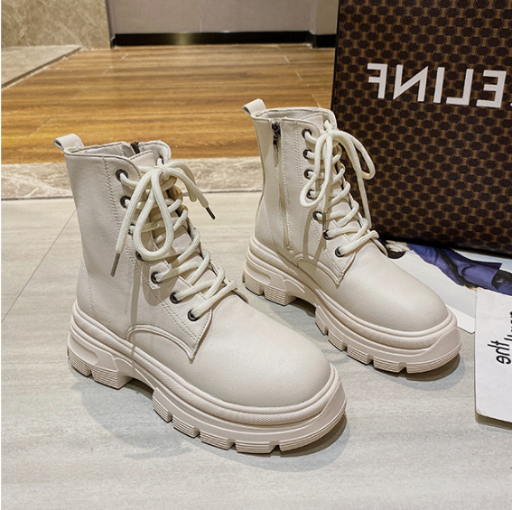 White lace-up boots on a light gray surface with a patterned bag in the background.