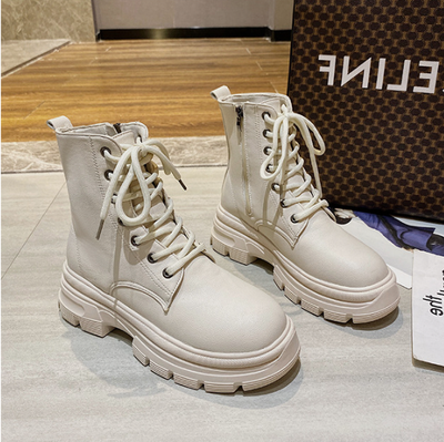 White lace-up boots on a light gray surface with a patterned bag in the background.