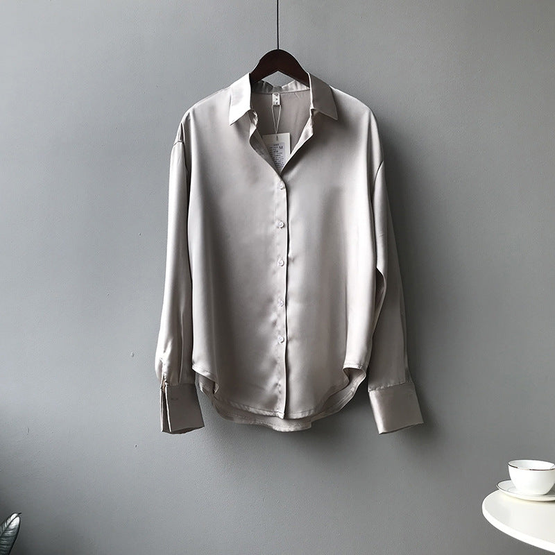 Light gray satin shirt on a hanger against a gray wall with a white table and cup in the corner.