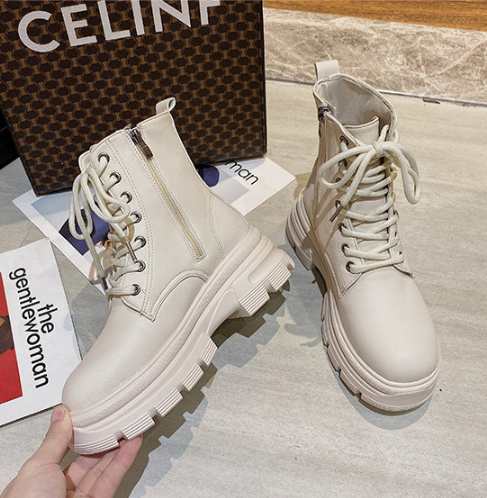 White boots with thick soles on a light gray surface, with a Celine bag in the background.