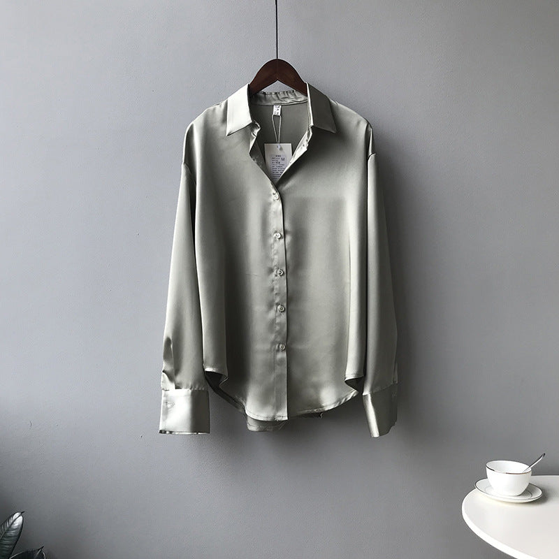 Light gray shirt on a hanger against a plain wall with a small table and cup in the corner.