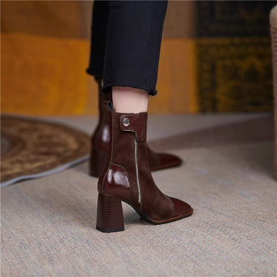 Brown ankle boots with a zipper detail worn by a person on a textured floor.