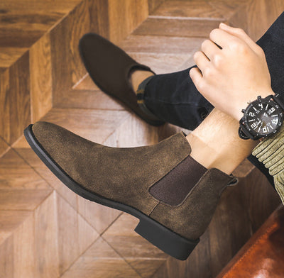 Brown suede Chelsea boots worn indoors on a wooden floor.