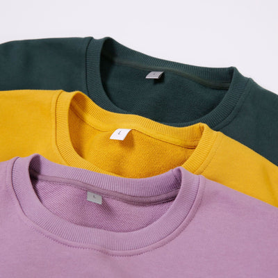 Three sweatshirts in green, yellow, and purple stacked on a light gray background