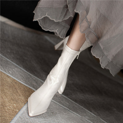 White ankle boots worn with a gray skirt on a wooden floor.