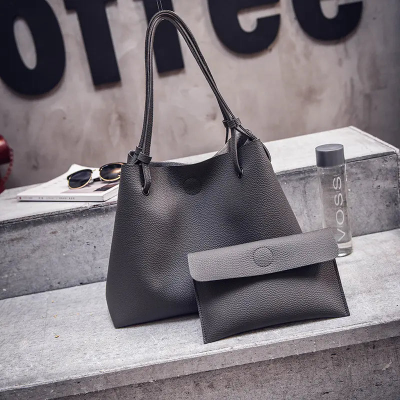 Gray handbag with a smaller pouch on a concrete surface with a blurred background