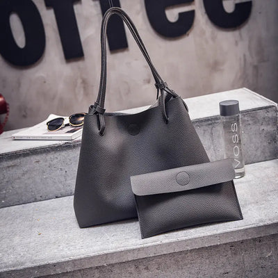 Gray handbag with a smaller pouch on a concrete surface with a blurred background