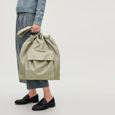 Person holding a light green drawstring bag on a plain background