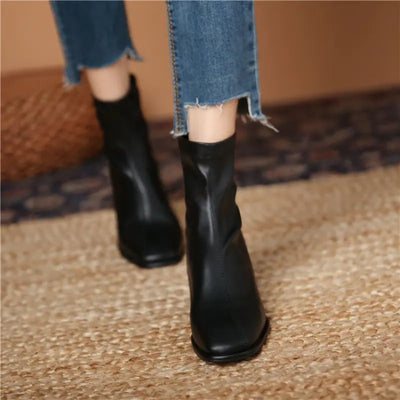 Black ankle boots worn with blue jeans on a textured floor.