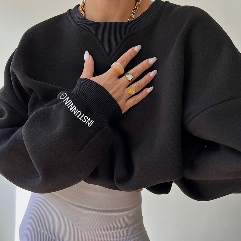 Person wearing a black sweatshirt with text, holding hands together in front of a neutral background