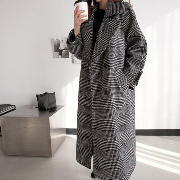 Person wearing a long plaid coat holding a coffee cup in an indoor setting.