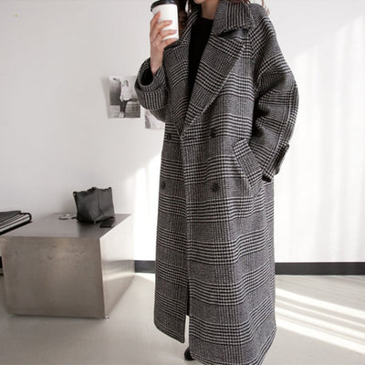 Person wearing a long plaid coat holding a coffee cup in an indoor setting.