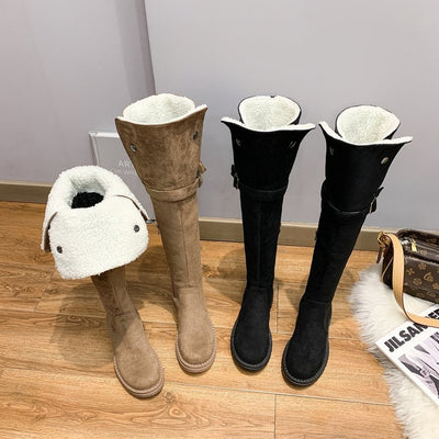 Pair of tan and black knee-high boots with white fur lining on a wooden floor.