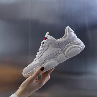White sneaker held by a hand against a blurred background