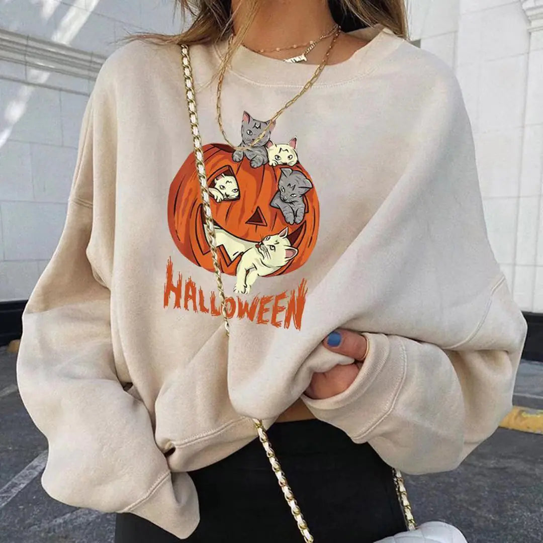 Person wearing a beige sweatshirt with a Halloween design featuring cats and a pumpkin.