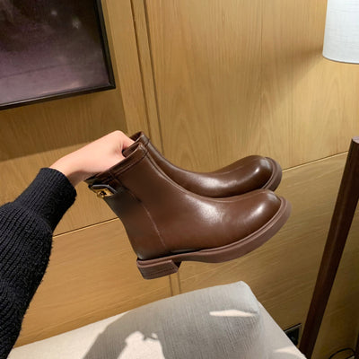 Brown leather boots held by a person against a wooden wall.