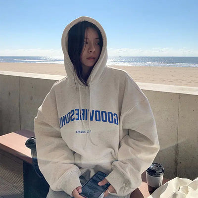 Person wearing a beige hoodie with 'GOODVIBES' text at the beach