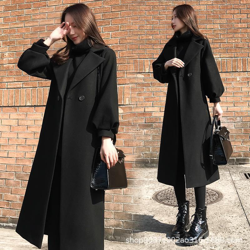 Woman wearing a black coat standing against a brick wall.