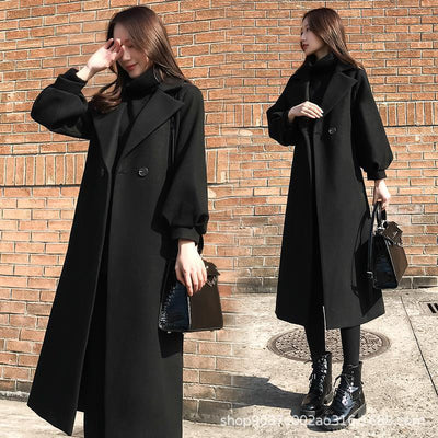 Woman wearing a black coat standing against a brick wall.