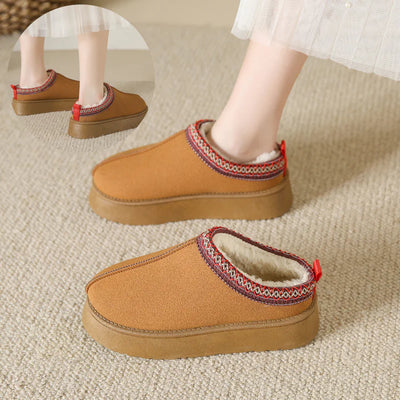 Brown slippers with decorative trim worn by a person on a beige carpet.