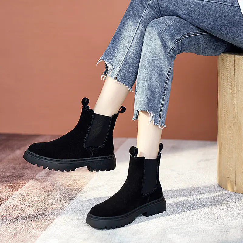 Black Chelsea boots worn with blue jeans and white socks on a neutral background