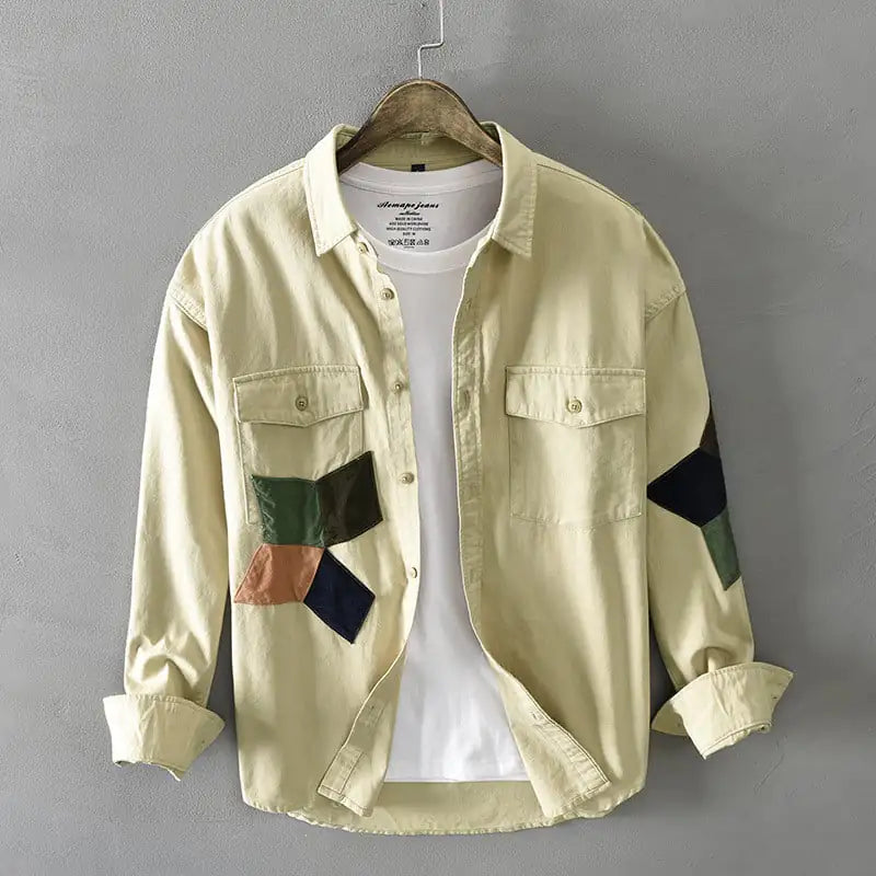 Light-colored shirt with patchwork sleeves on a hanger against a gray background