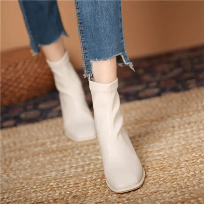 White ankle boots worn with blue jeans on a textured floor.