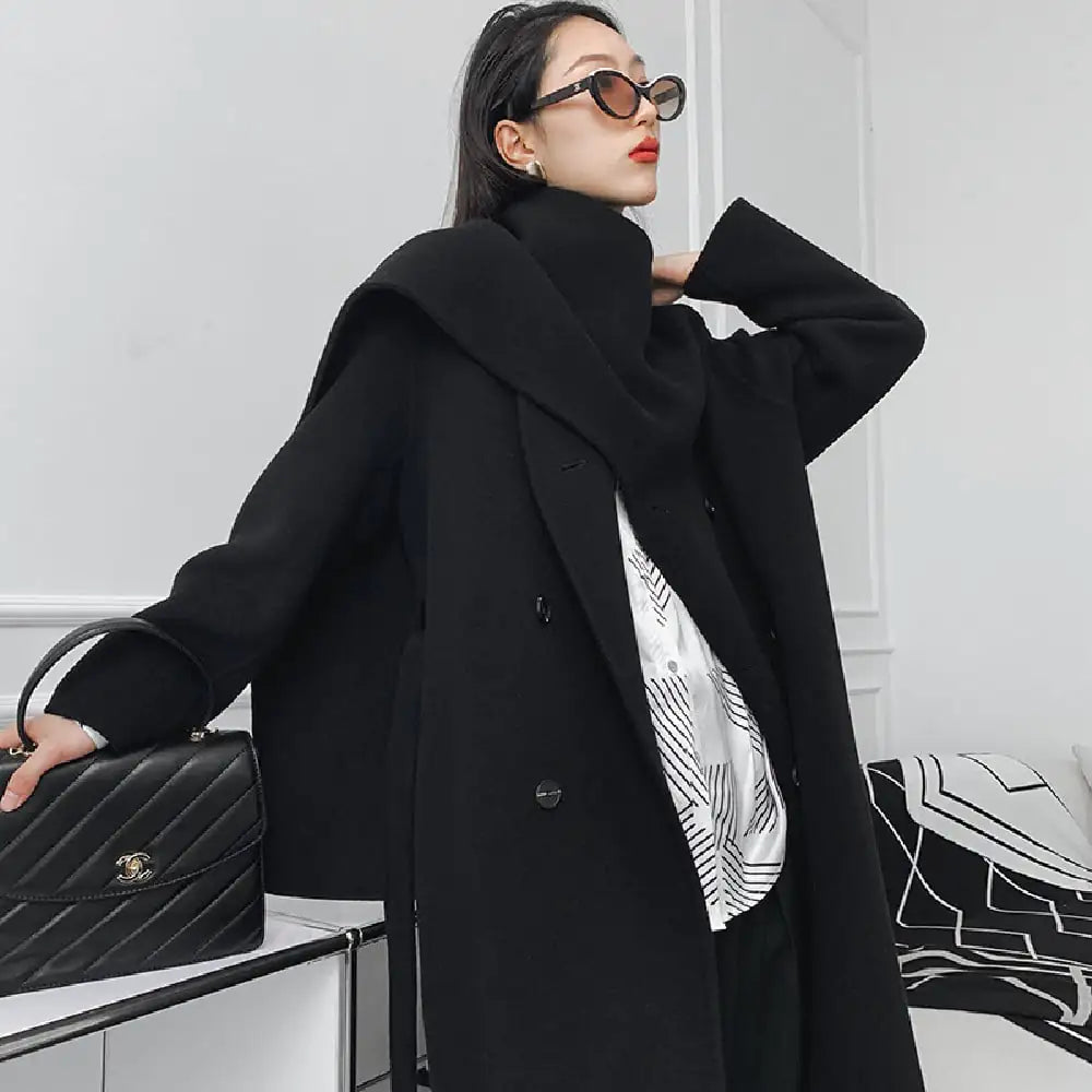 Person wearing a black coat holding a black handbag against a white background