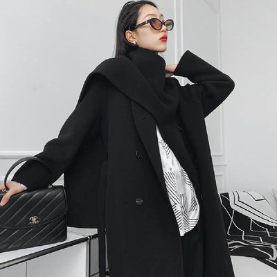 Person wearing a black coat holding a black handbag against a white background