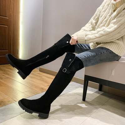 Person wearing black knee-high boots sitting on a bench indoors.