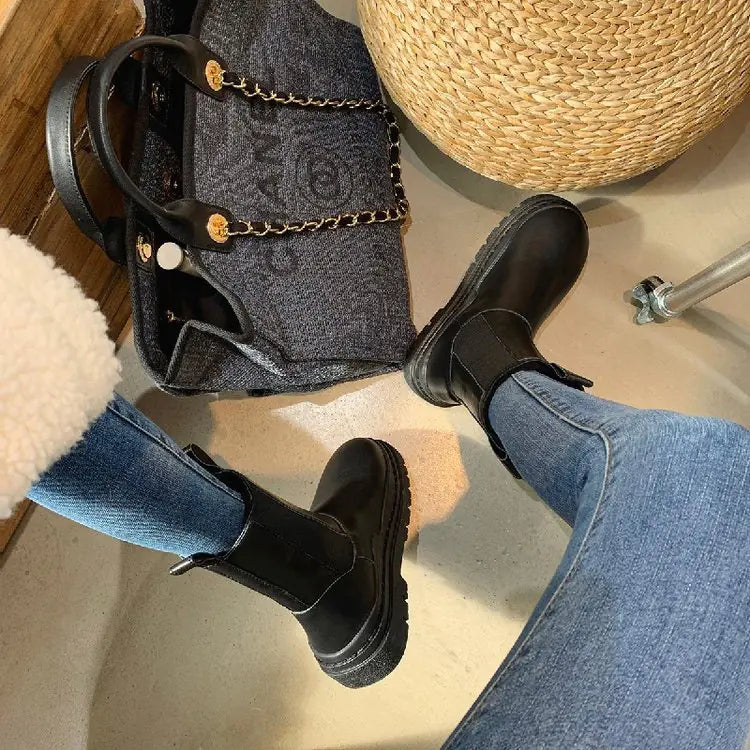 Person wearing black boots and blue jeans with a black handbag on a light surface.