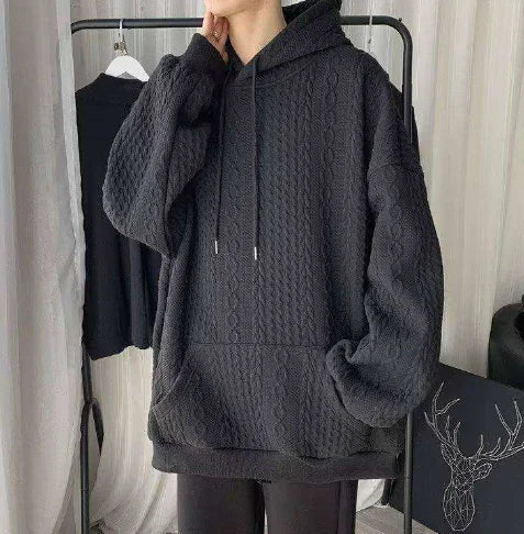 Person wearing a textured dark gray hoodie in a minimal indoor setting.