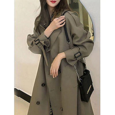 Woman wearing a long olive green coat holding a black handbag.