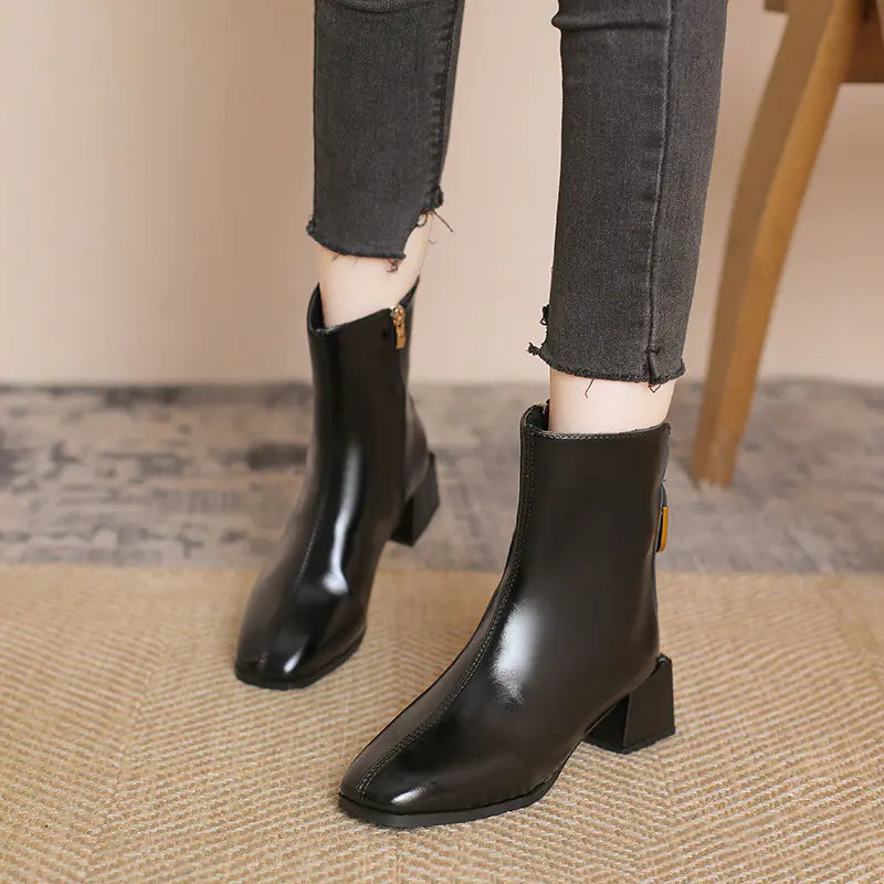 Black ankle boots worn with gray jeans on a neutral background