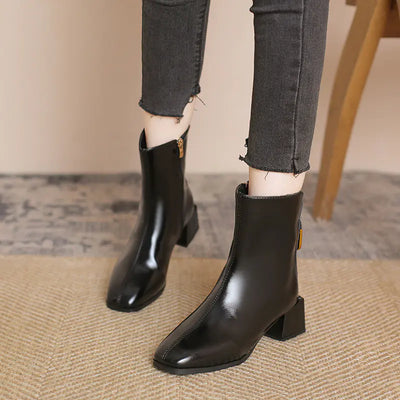 Black ankle boots worn with gray jeans on a neutral background