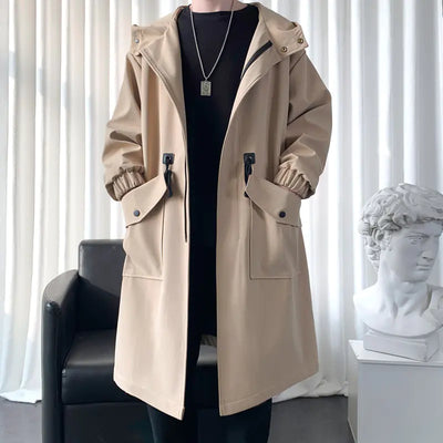 Person wearing a beige trench coat in a room with a black chair and white curtains.