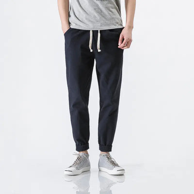 Person wearing navy jogger pants with a gray shirt and white sneakers on a white background