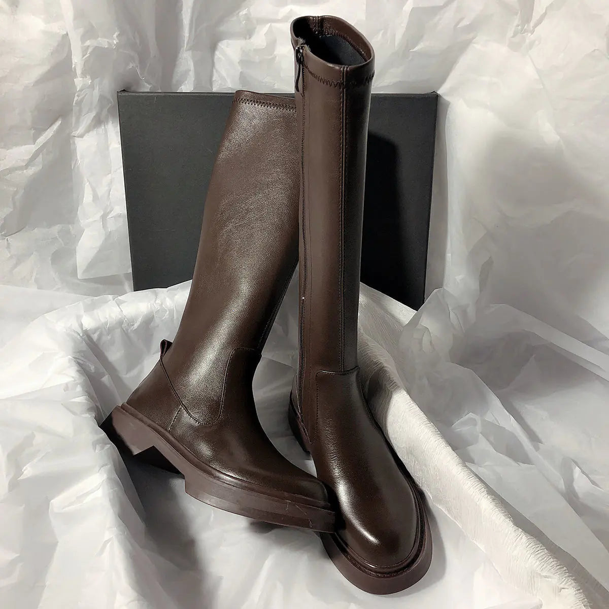 Pair of brown knee-high boots on a white textured surface