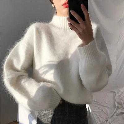 Person wearing a white sweater holding a phone with a blurred background
