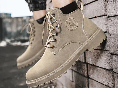 Beige boots with a brand logo worn by a person against a brick wall.
