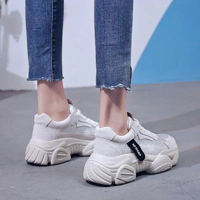 White sneakers worn with blue jeans on a neutral background