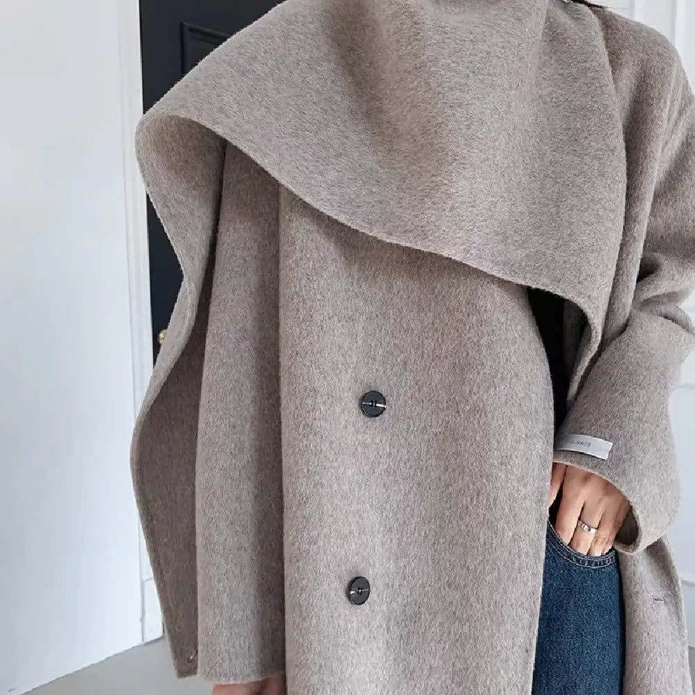 Close-up of a person wearing a gray coat with buttons, standing against a neutral background.