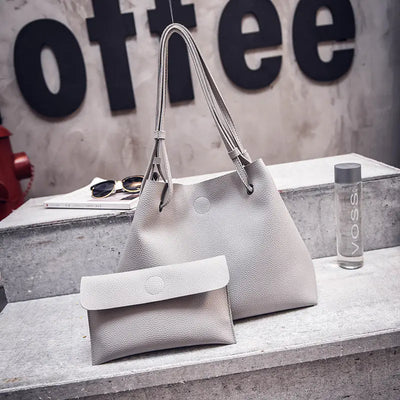 Gray handbag and clutch on a concrete surface with 'coffee' sign in the background