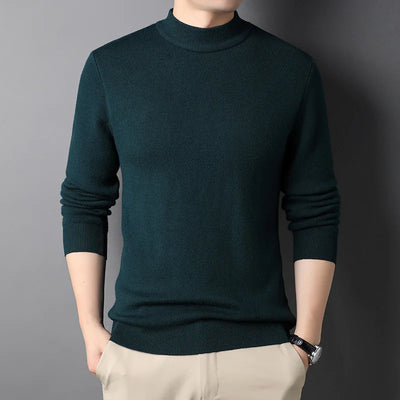 Person wearing a dark green turtleneck sweater against a gray background