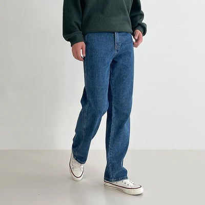Person wearing blue jeans and a green sweater on a plain background