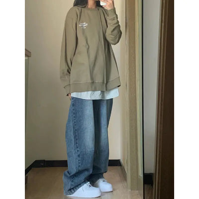 Person wearing a green oversized sweatshirt and blue jeans indoors.