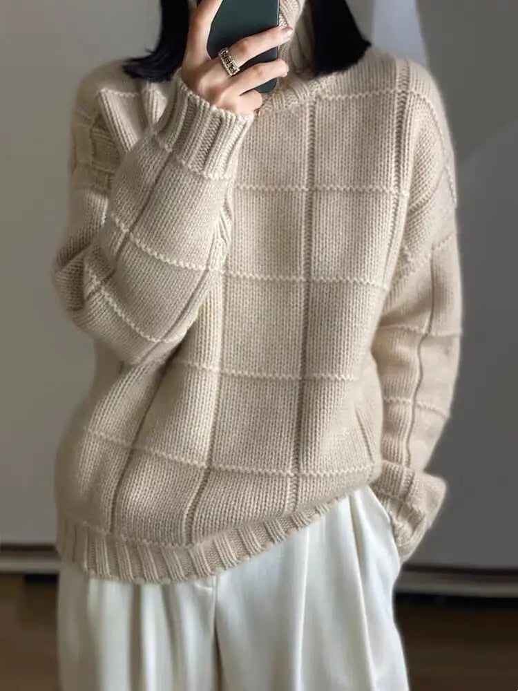 Person wearing a beige knitted sweater and white pants against a plain background