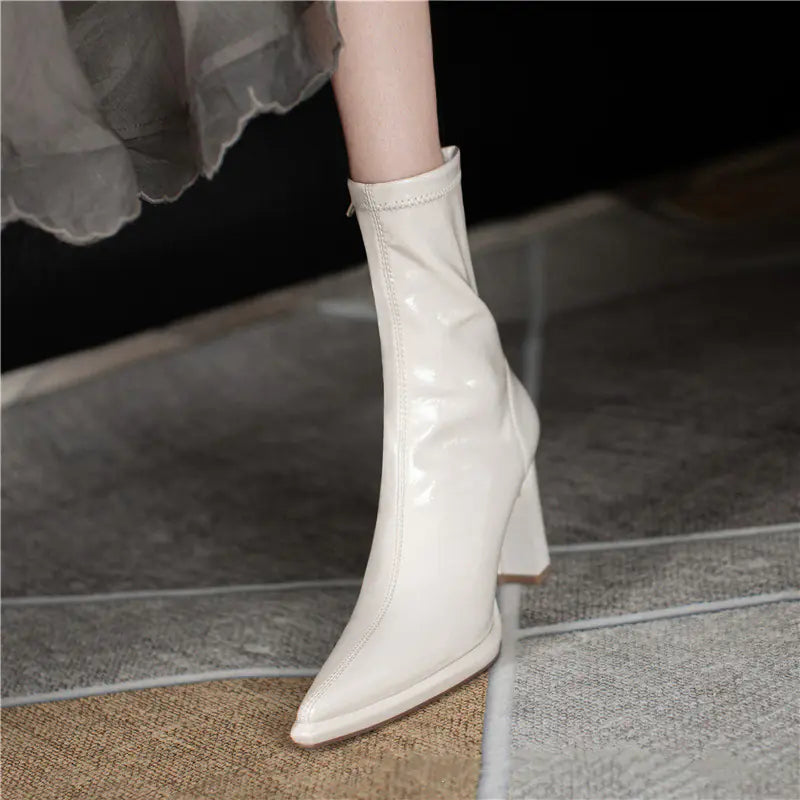 White high-heeled boots worn with a light skirt on a tiled floor.