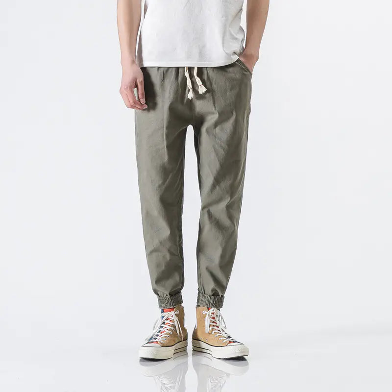 Person wearing olive green jogger pants and white sneakers on a white background