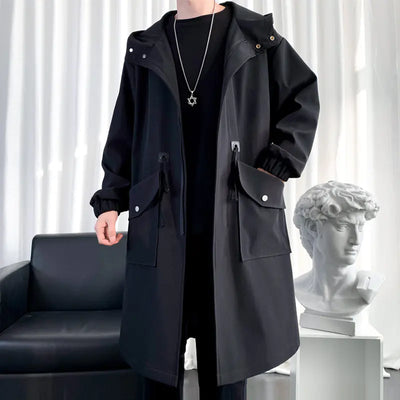 Person wearing a black trench coat in a room with a black sofa and white curtain.